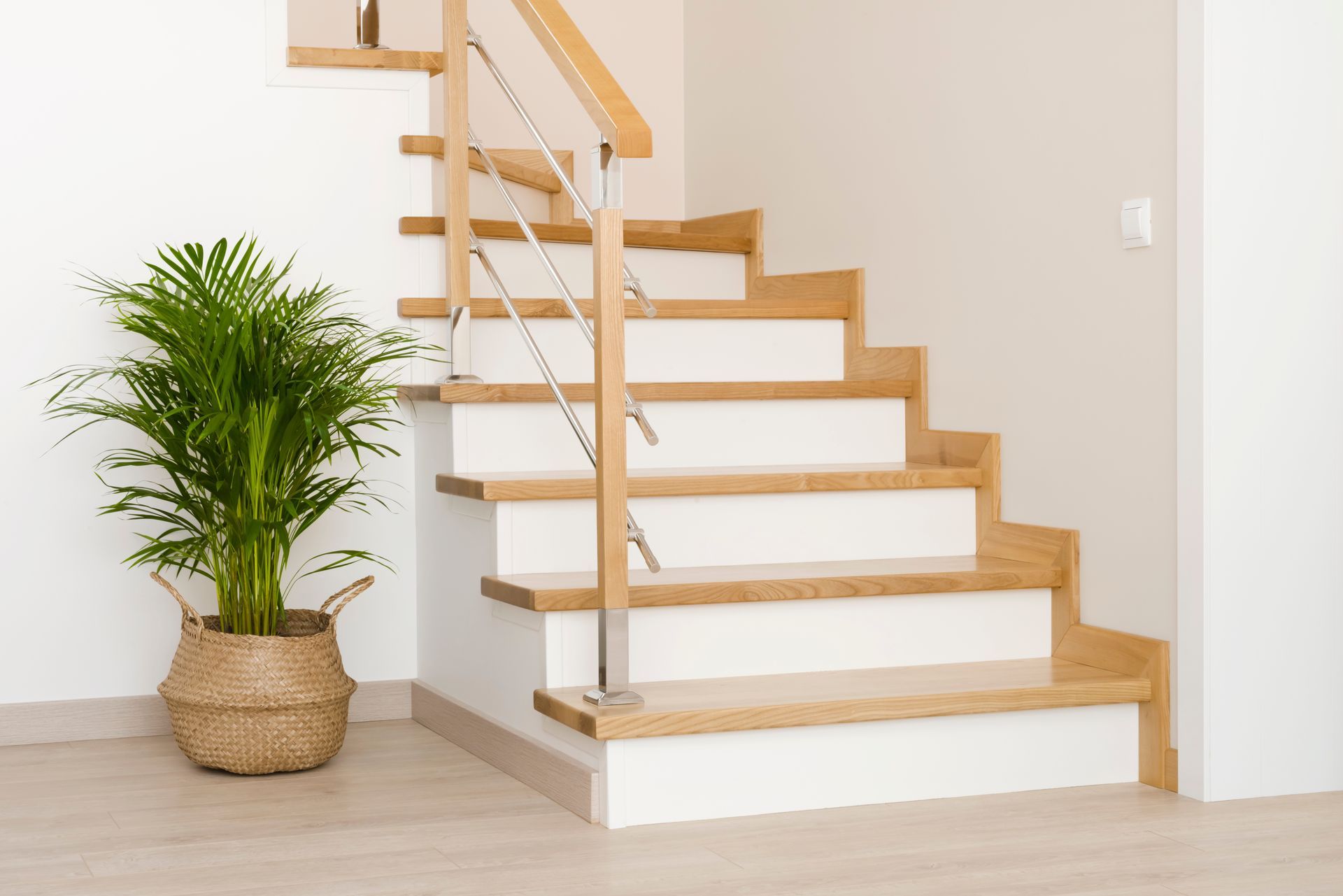 Wooden staircase with white risers, stainless steel railing, and a potted plant in a woven basket.