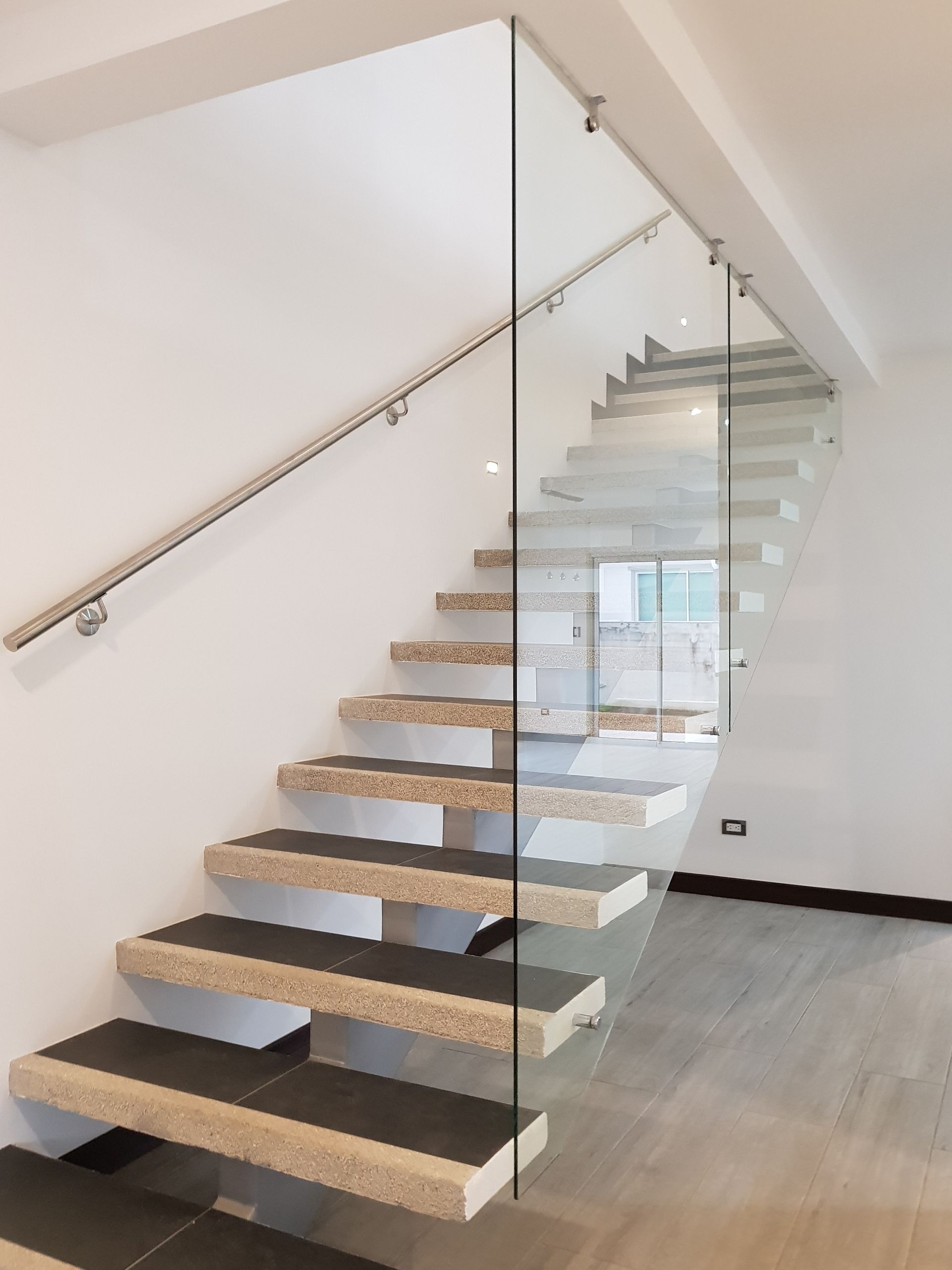 Modern staircase with stone treads, glass railing, and a wooden handrail.