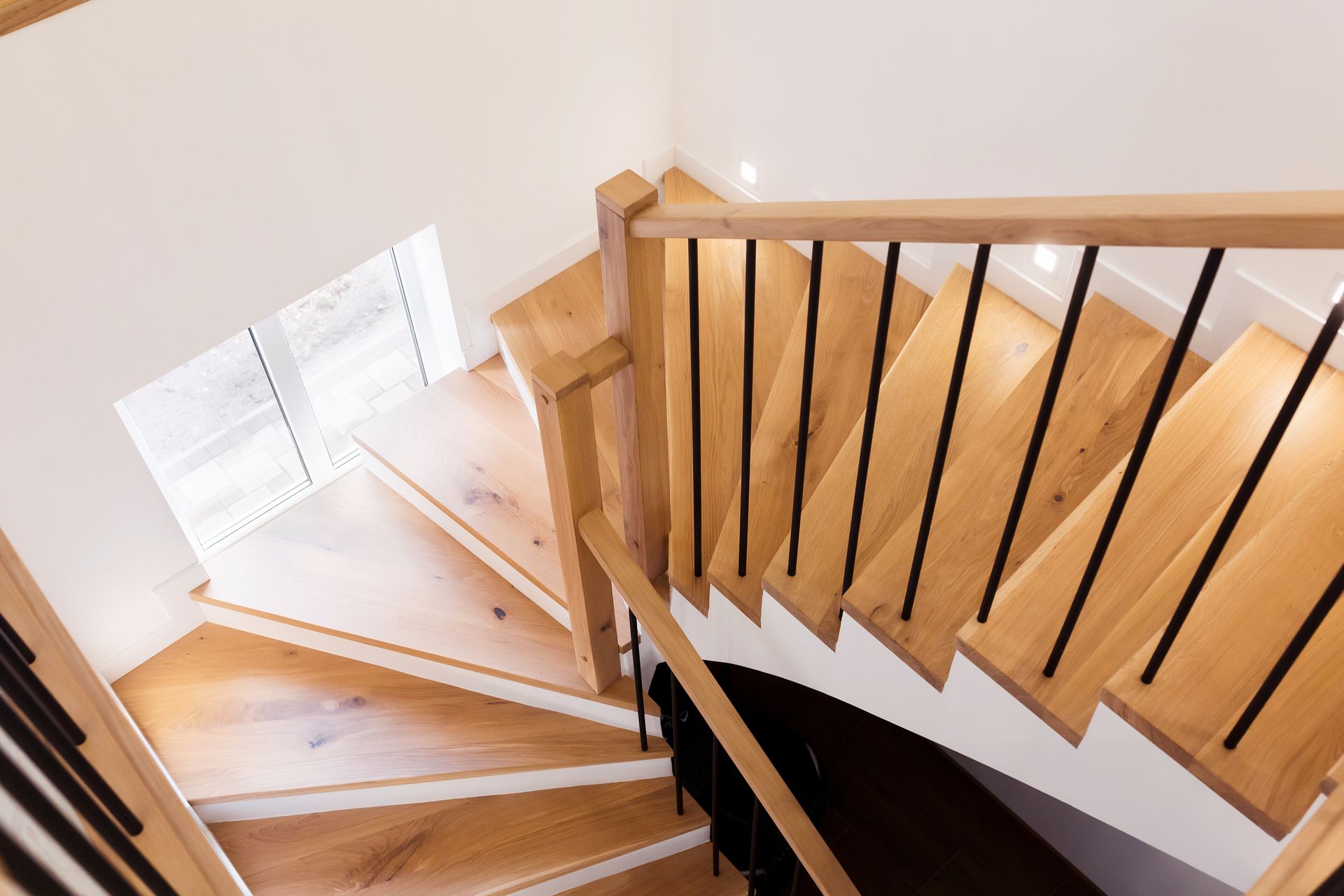 Wooden staircase with black metal railings, leading downwards, next to a window.