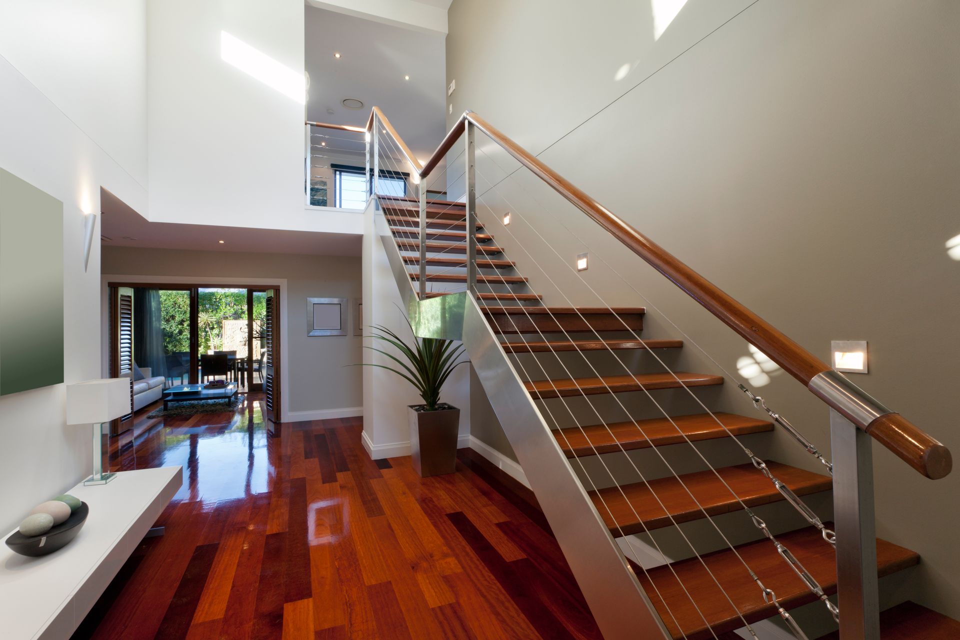 Wooden staircase with stainless steel supports and wooden railing in a modern home.