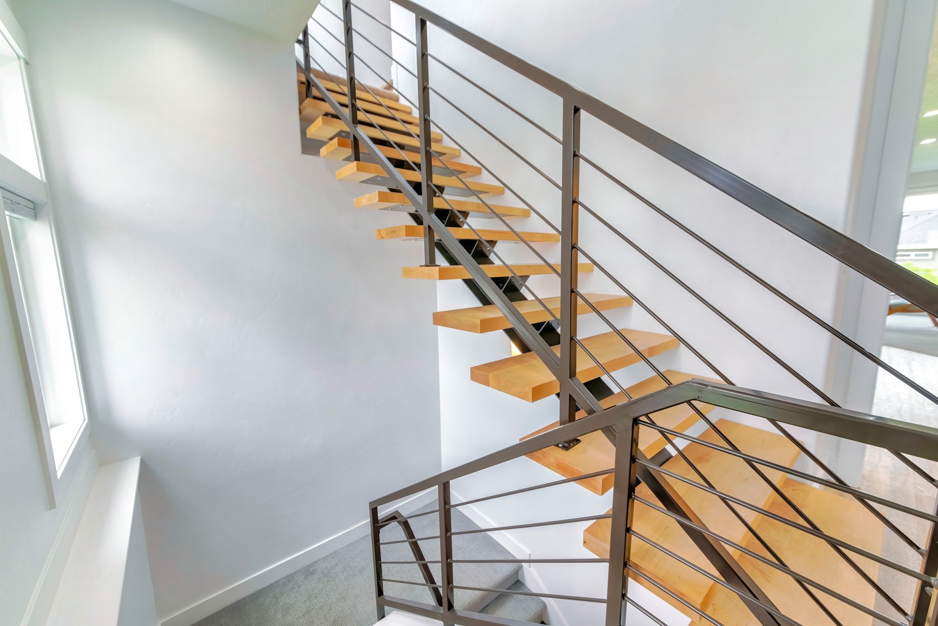 Wooden staircase with metal handrails against a white wall.