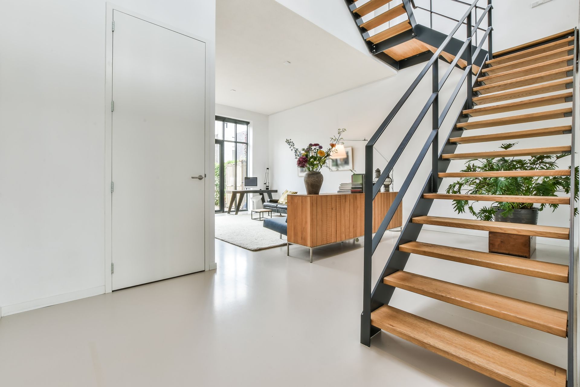 Modern interior with wooden staircase, neutral walls, and a view of a living room.