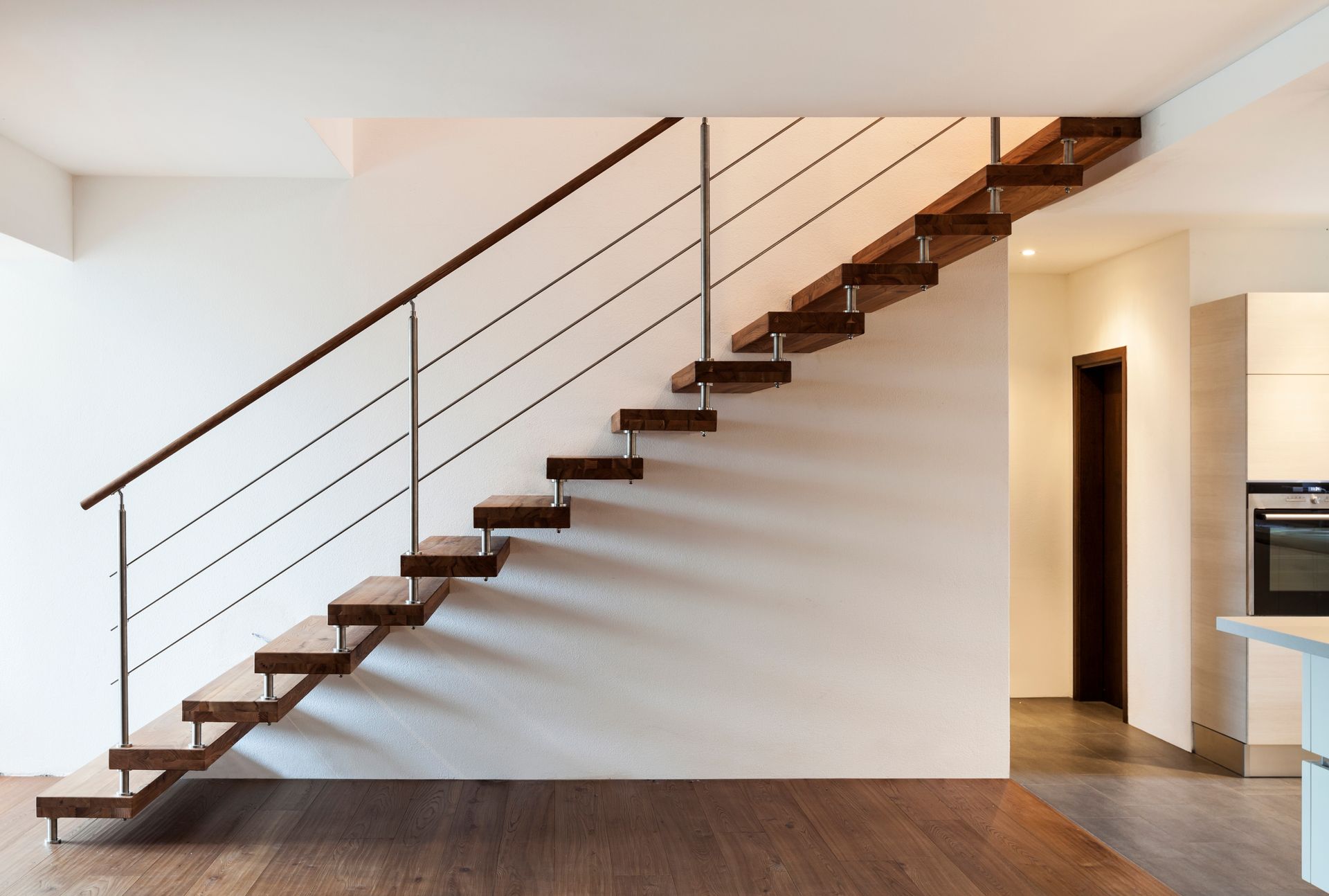Wooden staircase with metal railings against a white wall.