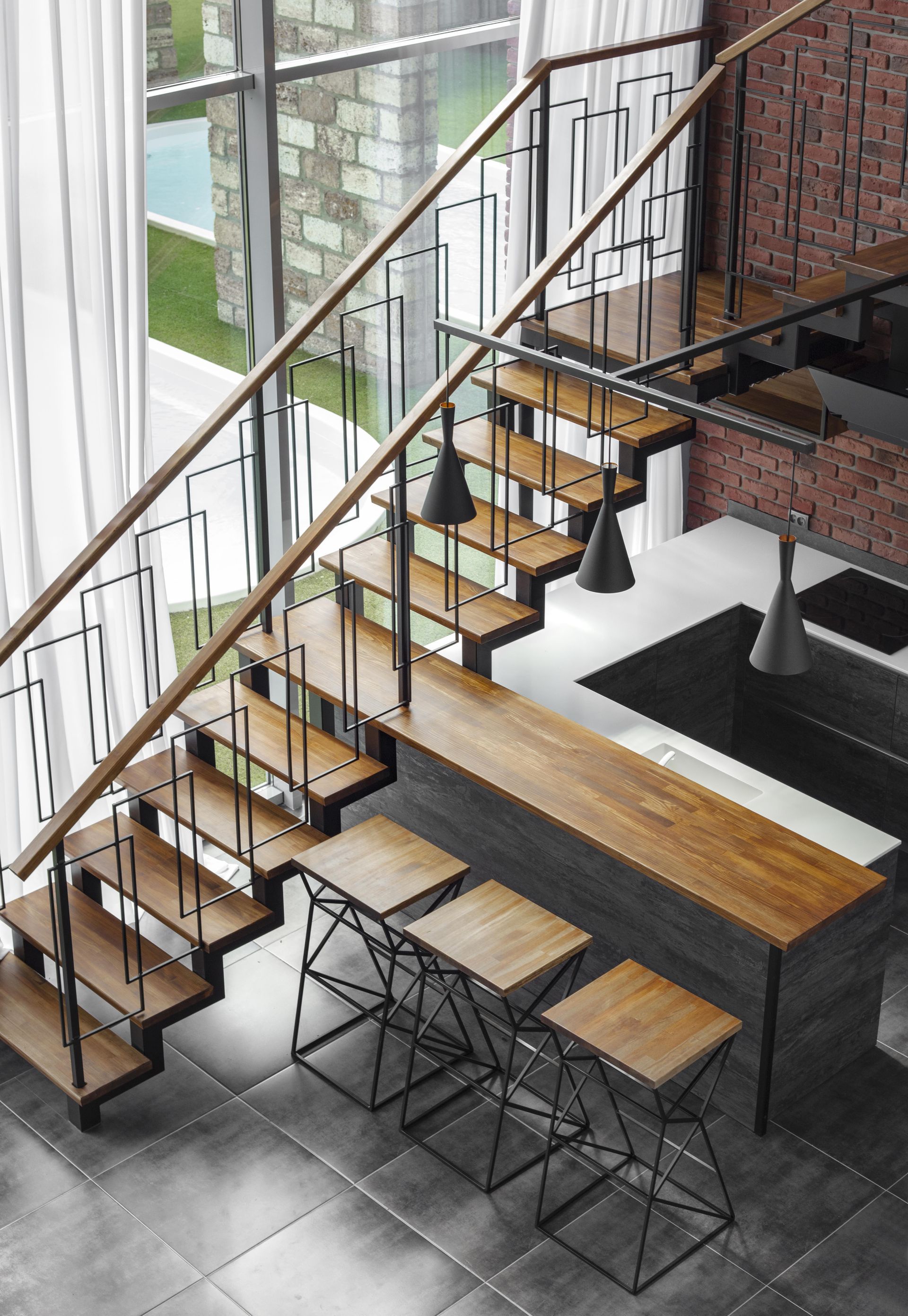 Staircase with wooden steps and black metal railings, overlooking a kitchen with a bar and stools.