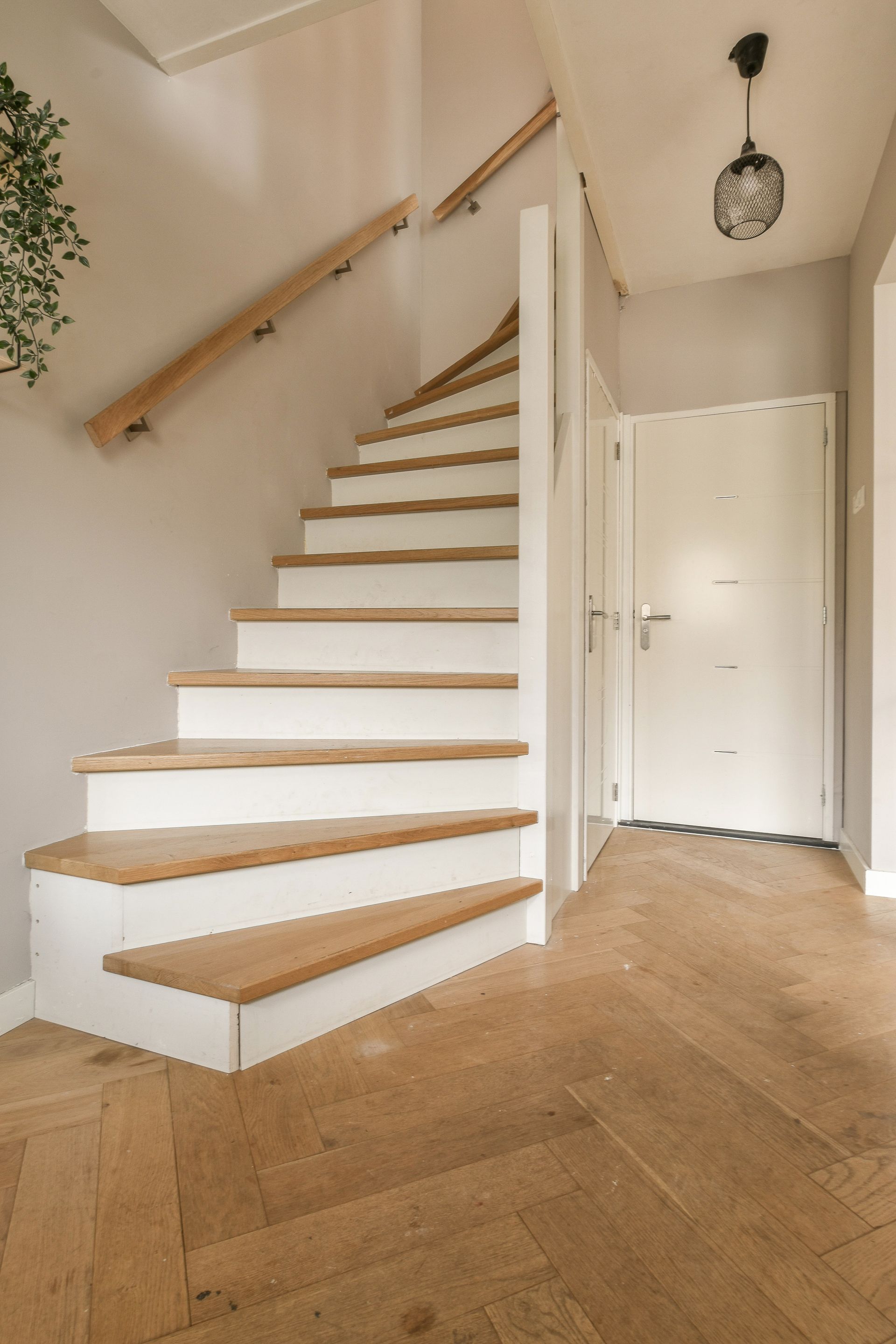 Staircase with wooden steps and handrail, white risers, and a white door in the background.