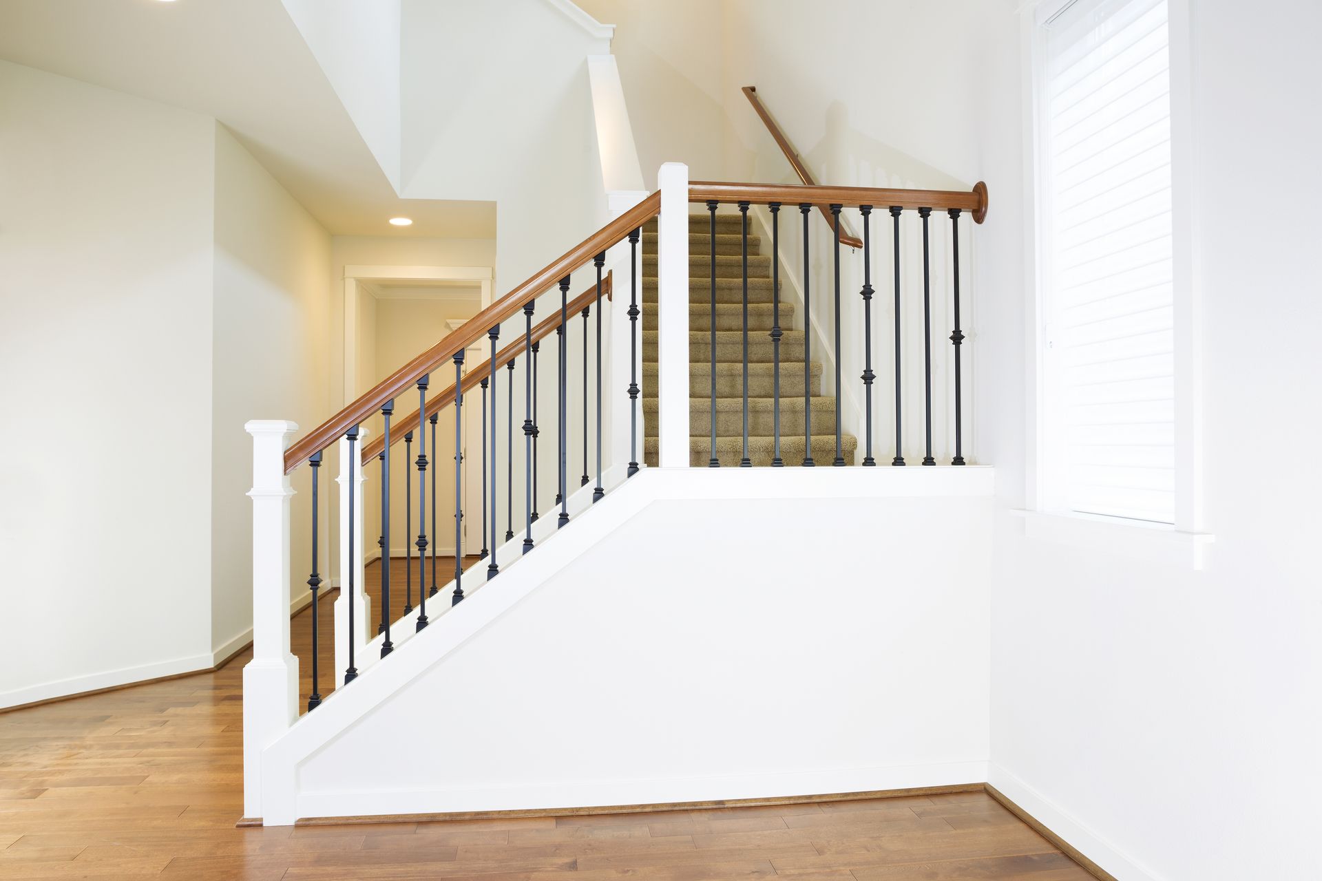 Staircase with wooden handrails and black spindles, ascending to a second floor. White walls, brown flooring.