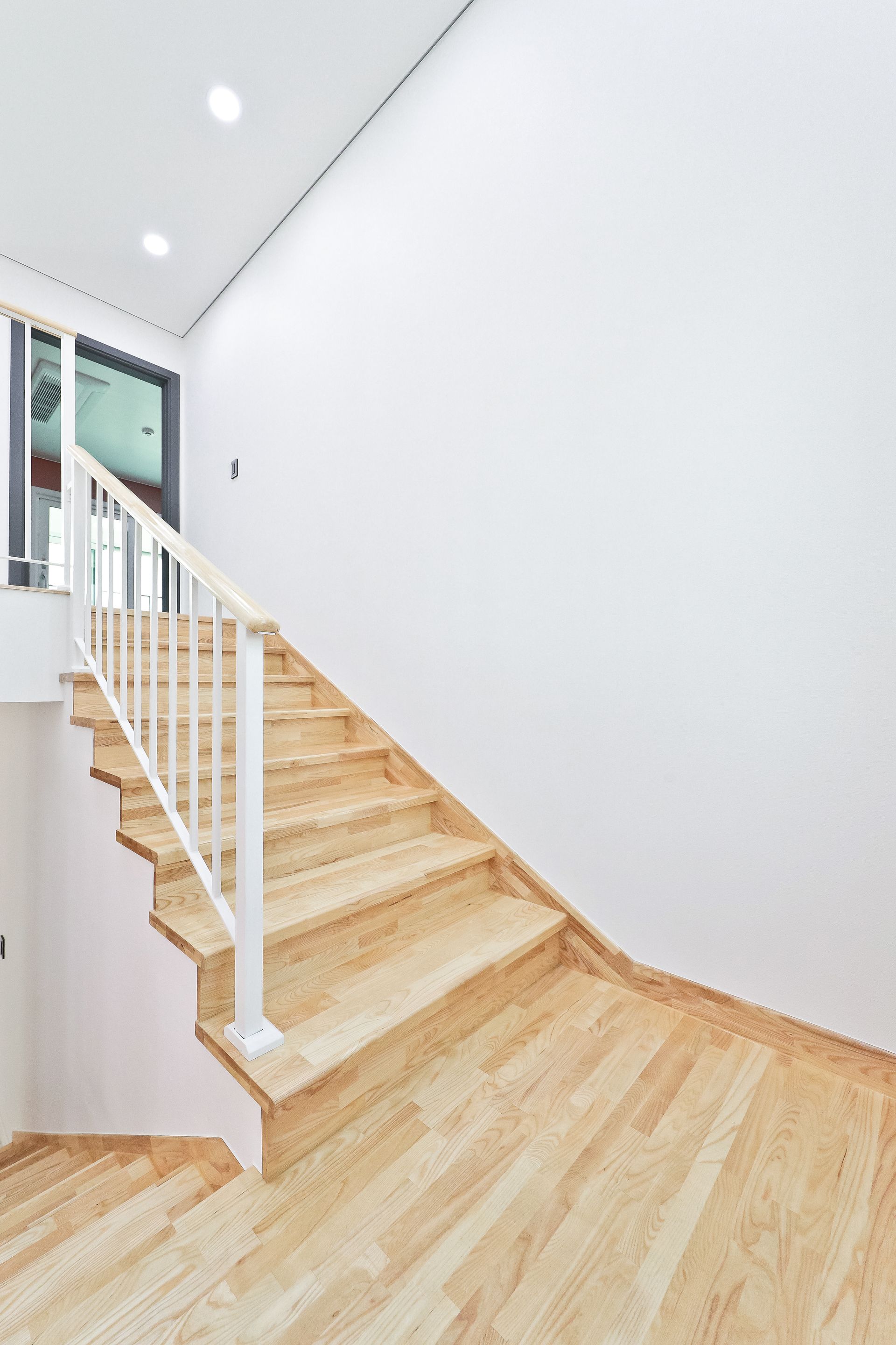Wooden staircase with white railing against a white wall in a modern home.