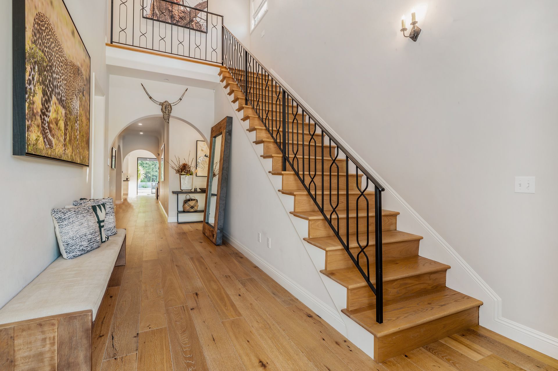 Entryway with wooden floors, staircase, bench, artwork, and arched doorway.
