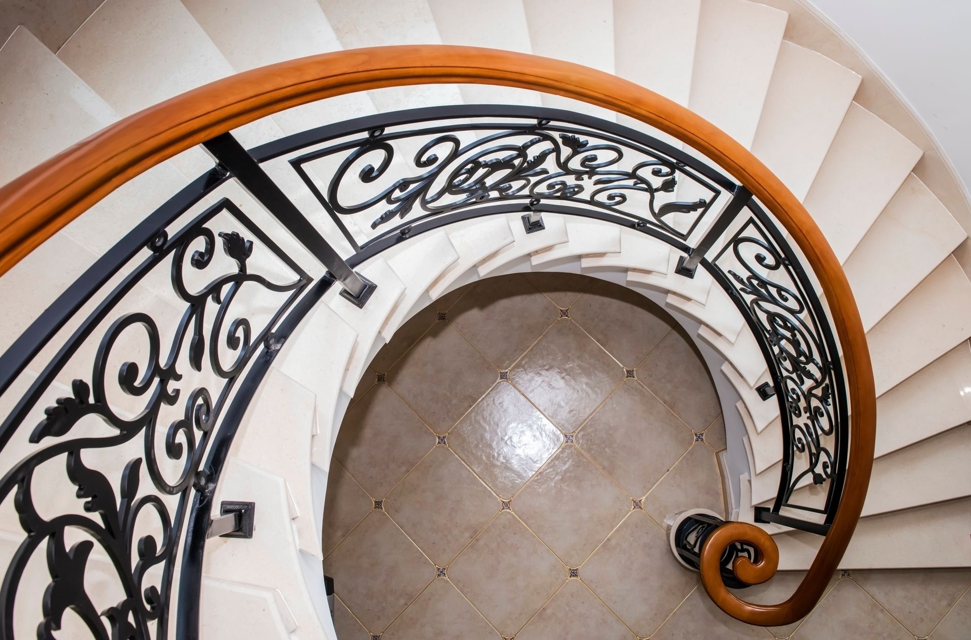 Spiral staircase with ornate wrought iron railing and wooden handrail.