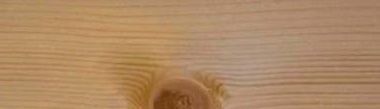 Close-up of a wooden surface with visible grain and a knot, showing natural wood color and texture.