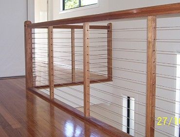 Wooden railing with horizontal metal cables, in a home.