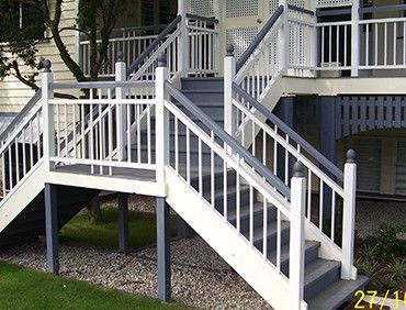 Exterior wooden staircase painted white and gray, leading up to a house.