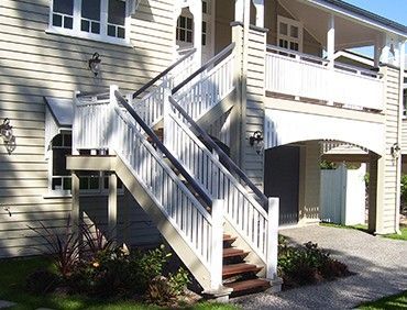 Exterior wooden staircase with white railings and dark wood steps leading to a house.