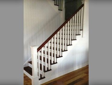 Staircase with white balusters and brown handrail. Wooden steps and wall, with a light gray background.