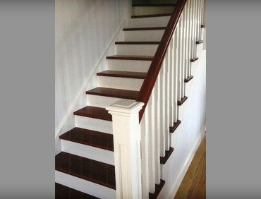 Wooden staircase with white spindles, dark wood steps, and a brown handrail.