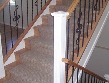 Staircase with carpeted steps, wooden accents, and black wrought iron balusters.