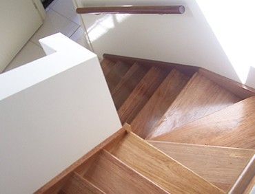 Wooden staircase with light brown treads and a white wall, viewed from above.