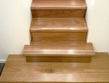Wooden staircase with three visible steps, in a hallway with white walls and a carpet.