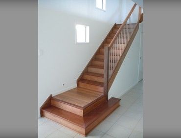 Wooden staircase with railing, leading up to a second floor, set against white walls and a tiled floor.