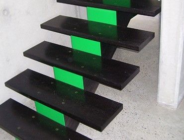 Black wooden stairs with green supports against a light-colored wall.