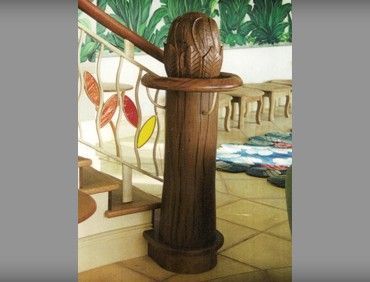 Wooden stair post with decorative carving and attached railing with colorful glass accents.
