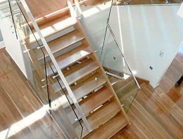 Wooden staircase with glass railing. Sunlight reflects on the wood floor and steps.