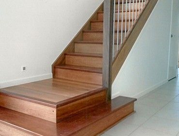Wooden staircase with a handrail, against white walls.