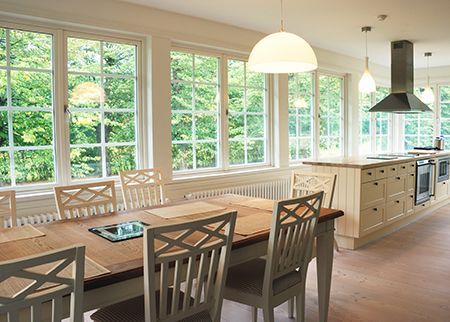 Bright dining room with large windows, wooden table, benches, and modern kitchen island