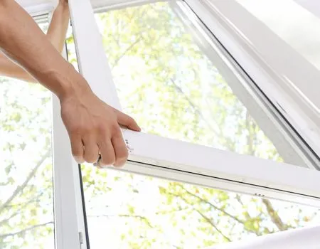 Hands opening a white window frame with bright daylight outside