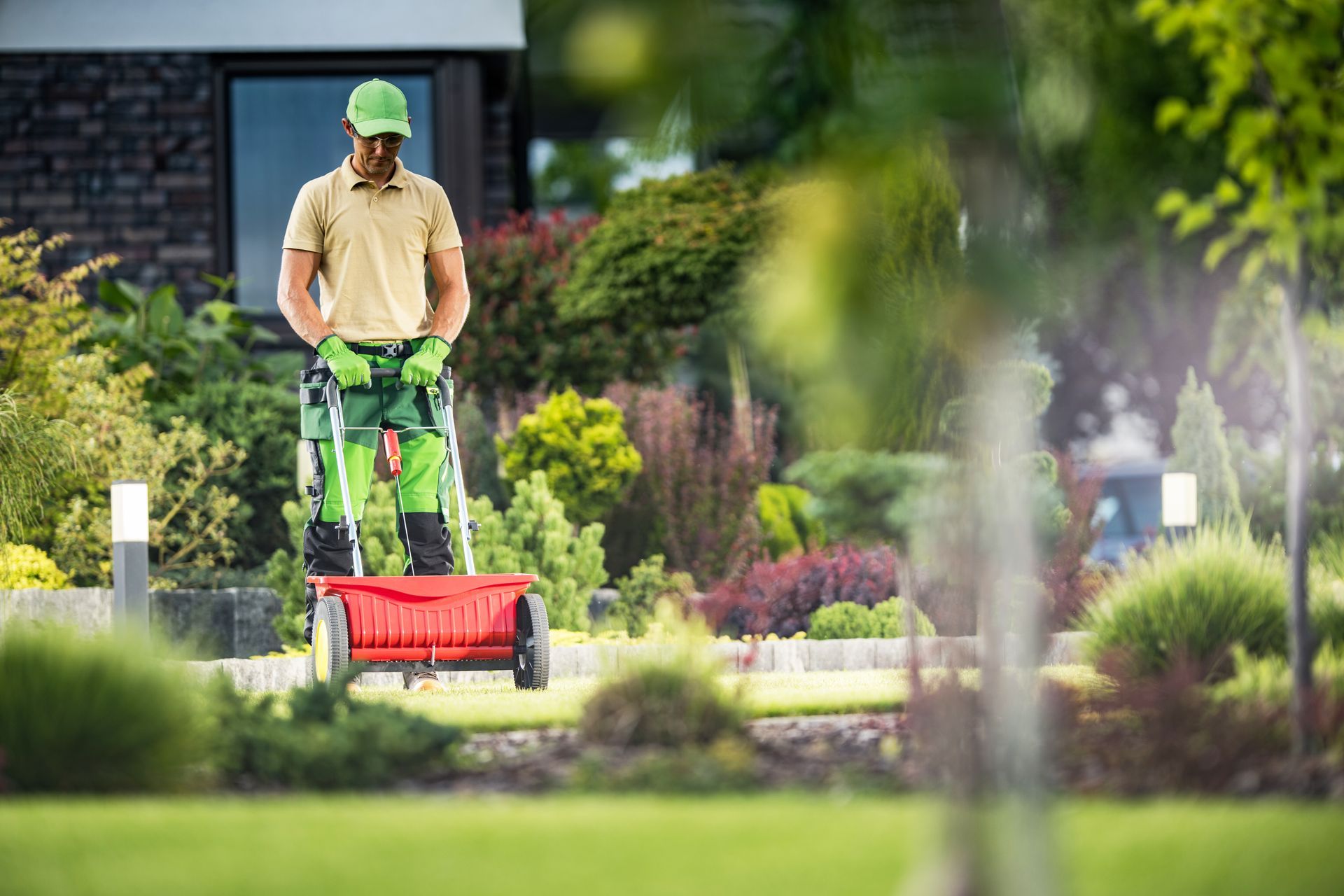 Person mowing a lawn with a red push mower in a garden-lined yard