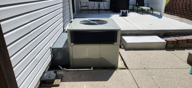 Outdoor HVAC unit beside a house on a concrete patio, with steps and siding visible nearby.