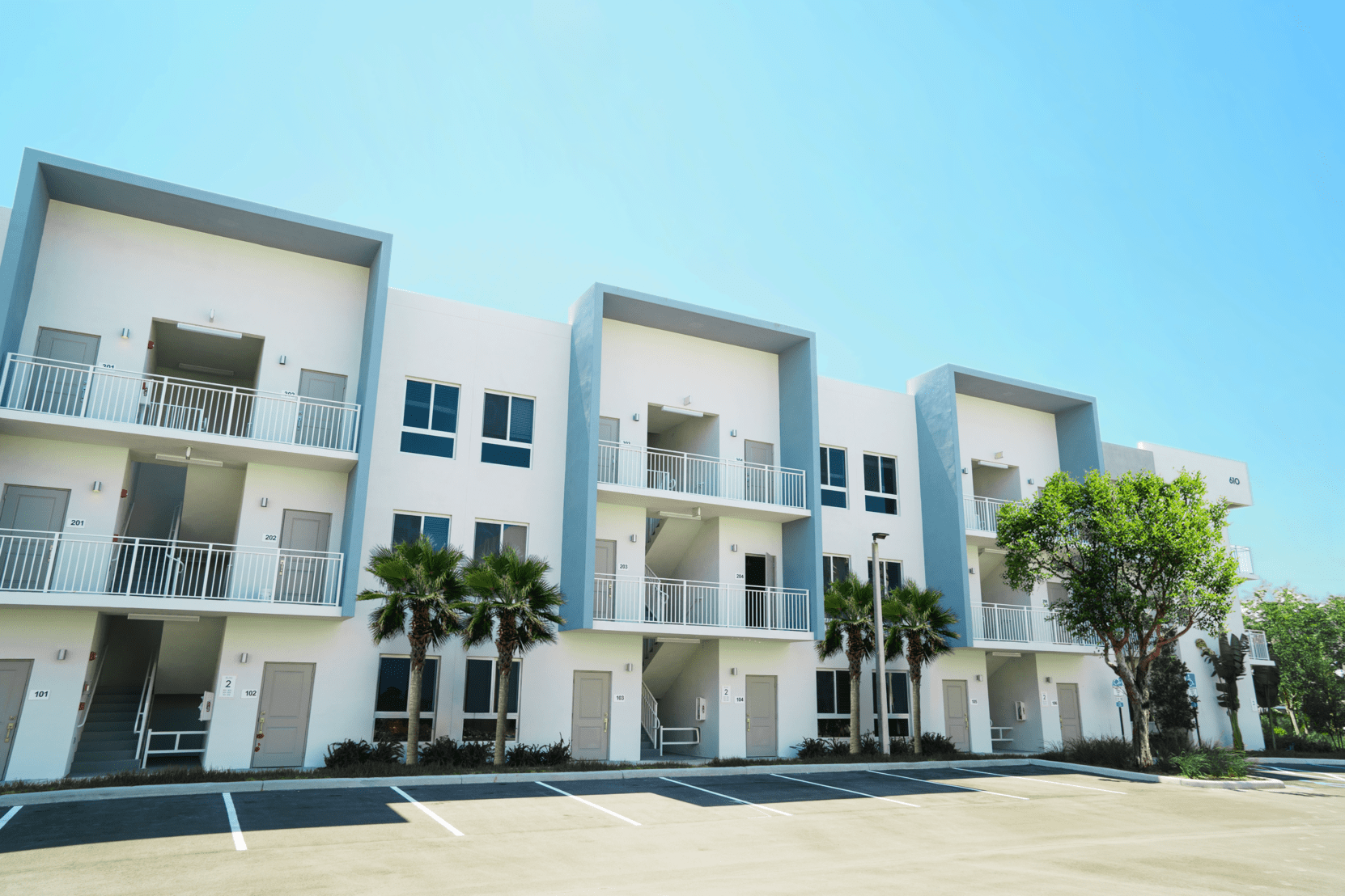 Modern white apartment buildings with balconies under a clear blue sky at Atlantica at Dania Beach apartments in Dania Beach, FL.