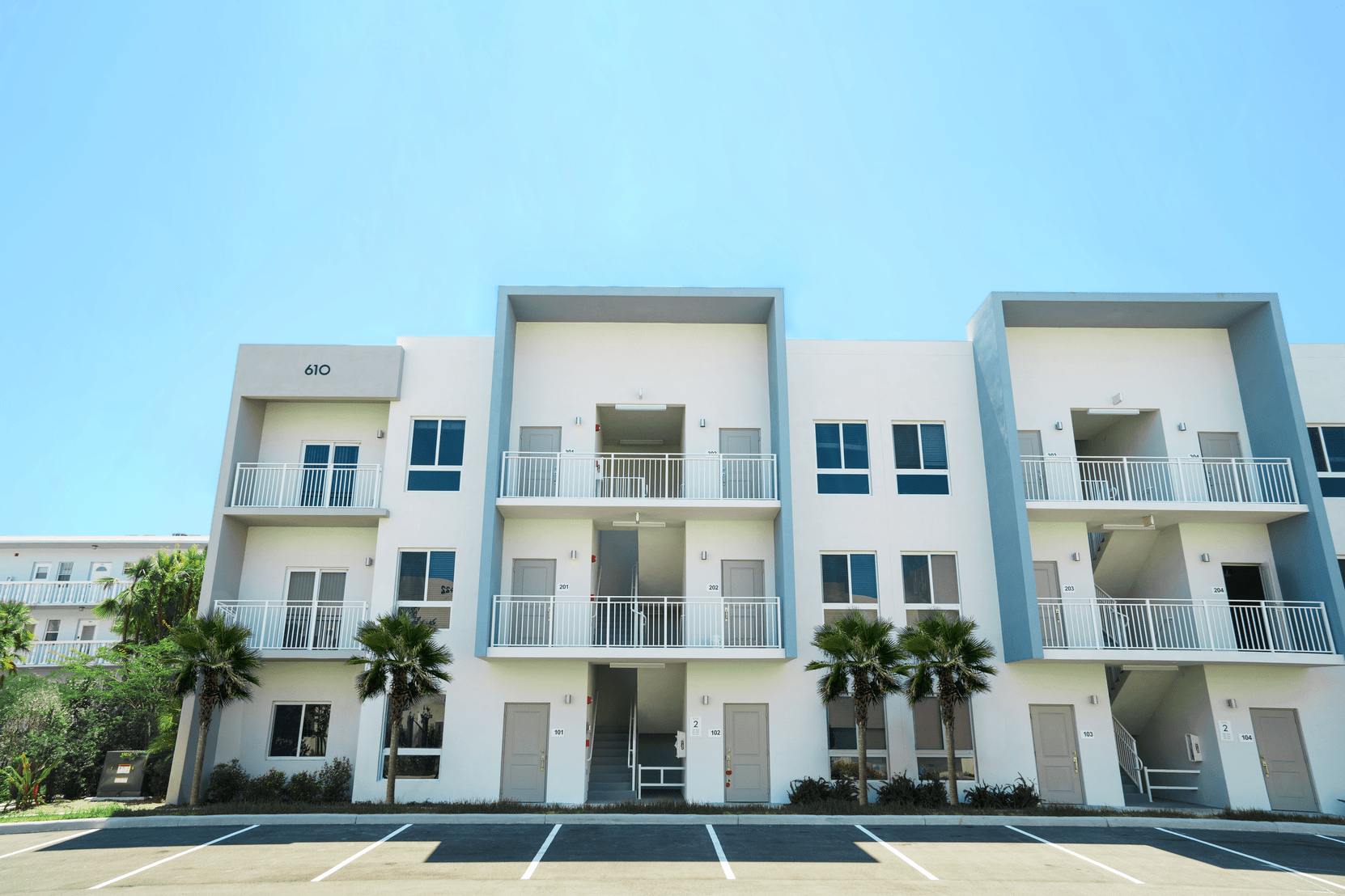 Three-story apartment building with balconies and parking spaces under a clear blue sky at Atlantica at Dania Beach apartments in Dania Beach, FL.