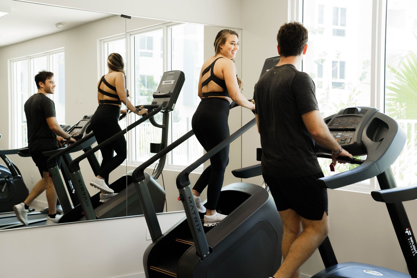 People exercising on treadmills in a bright gym, with mirrors and large windows at Atlantica at Dania Beach apartments in Dania Beach, FL.