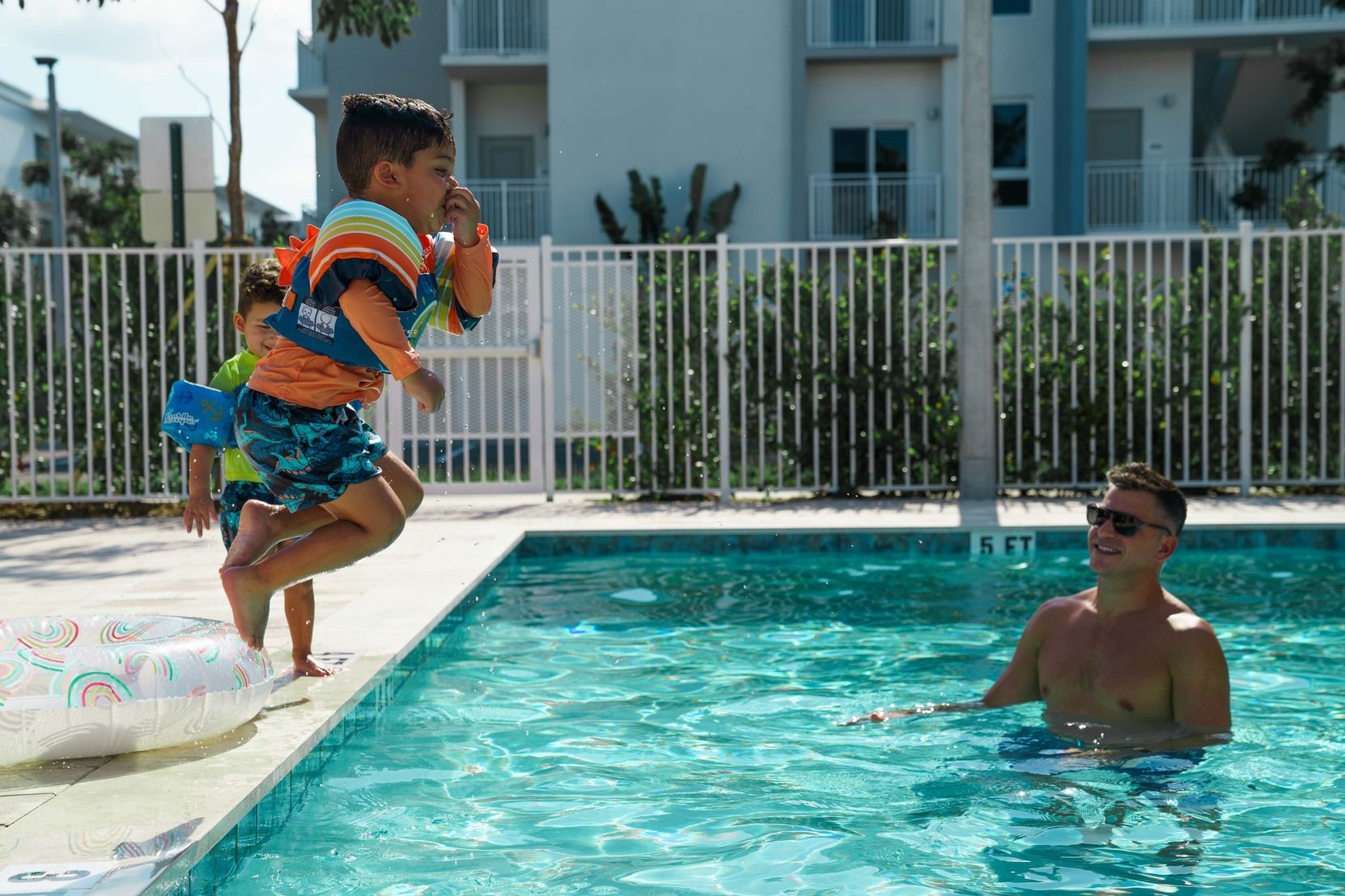 Child jumping into a swimming pool toward a man in the water at a sunny resort pool at Atlantica at Dania Beach apartments in Dania Beach, FL.