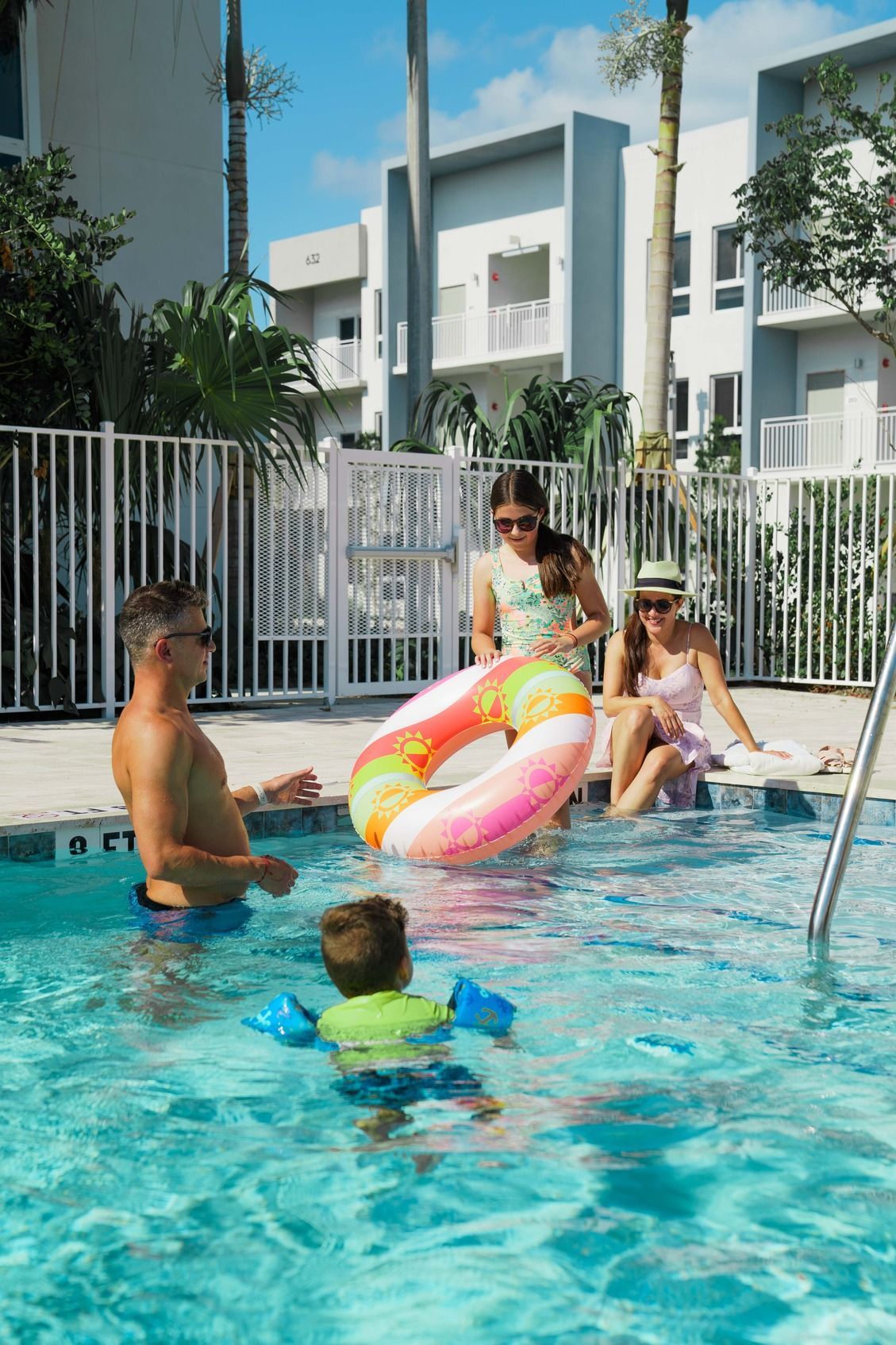 People relaxing and playing in a bright outdoor swimming pool with floaties at an apartment complex at Atlantica at Dania Beach apartments in Dania Beach, FL.