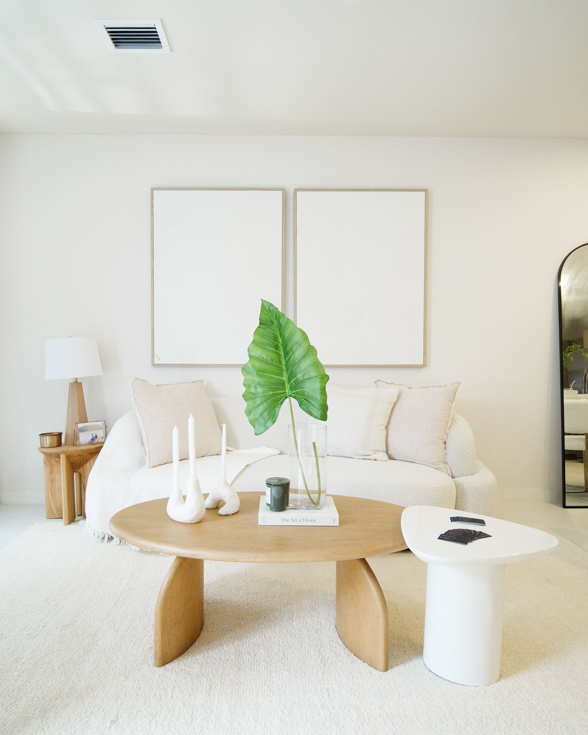 Bright minimalist living room with white sofa, wood coffee table, and green leaf decor at Atlantica at Dania Beach apartments in Dania Beach, FL.