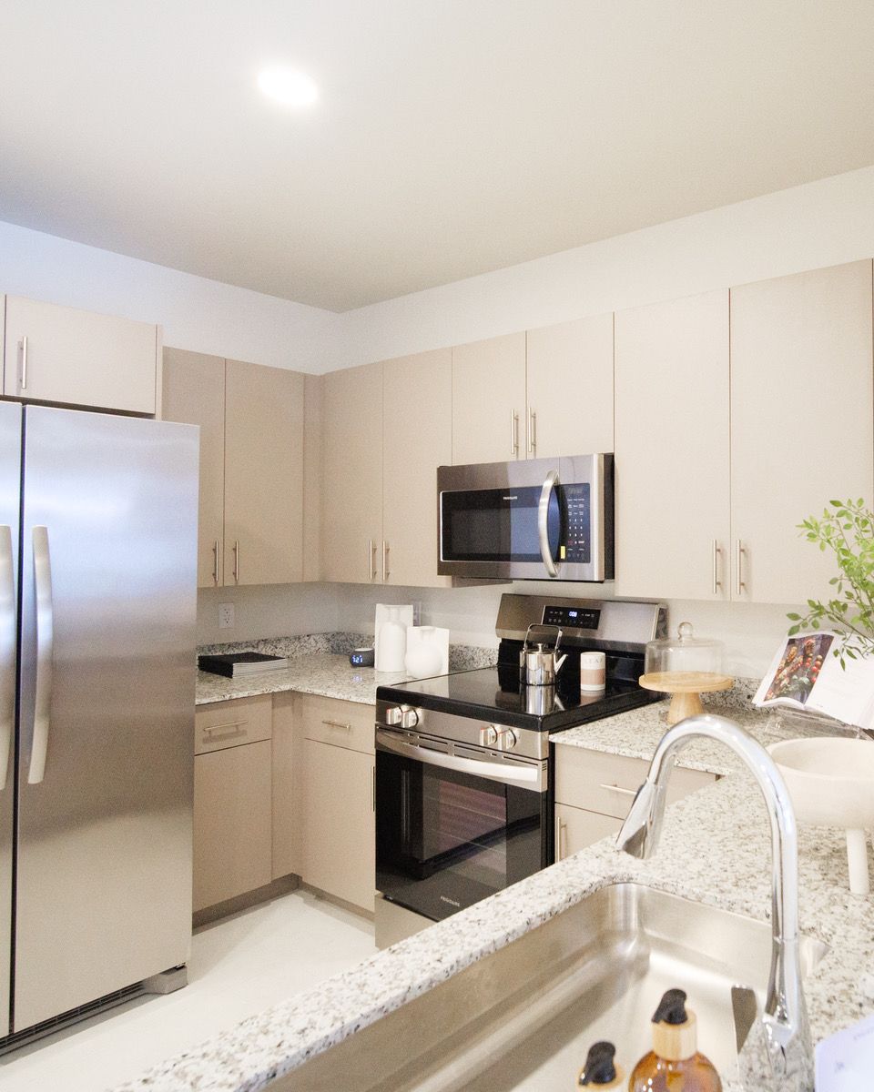 Modern white kitchen with stainless steel appliances and granite countertops, viewed from the sink at Atlantica at Dania Beach apartments in Dania Beach, FL.