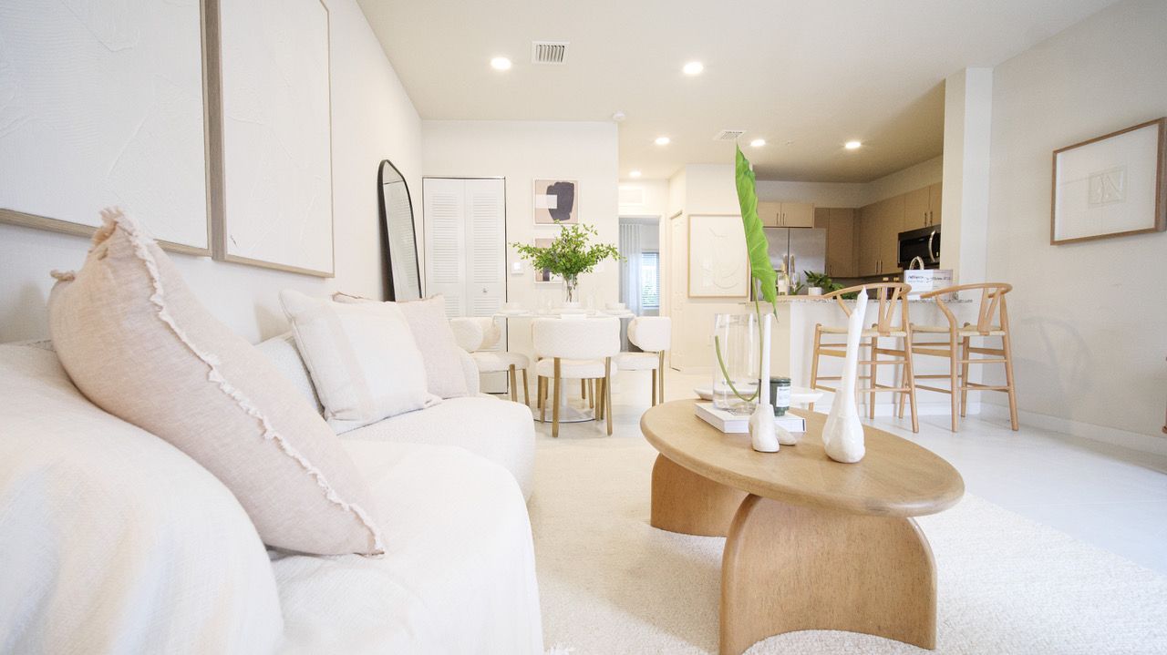 Bright minimalist living room with white sofa, round wooden coffee table, and dining area in the background at Atlantica at Dania Beach apartments in Dania Beach, FL.