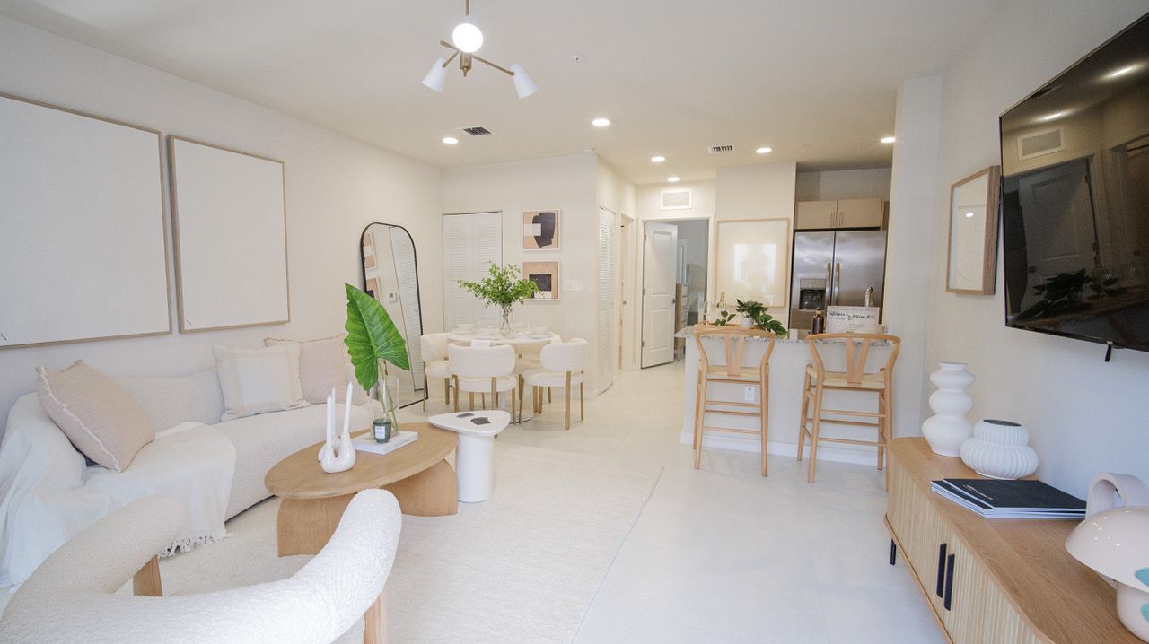 Bright, airy living room with white furniture, dining table, plants, and wall-mounted TV at Atlantica at Dania Beach apartments in Dania Beach, FL.