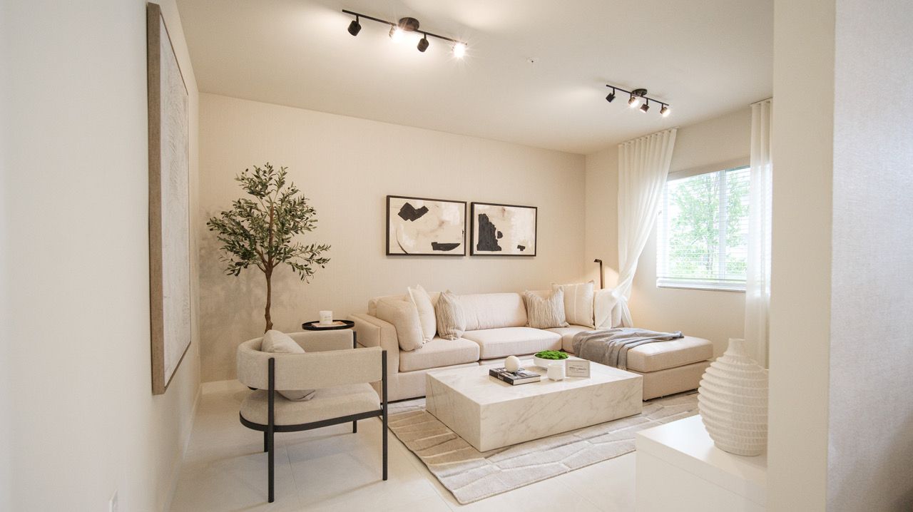 Bright beige living room with sectional sofa, armchairs, coffee table, and wall art under track lighting at Atlantica at Dania Beach apartments in Dania Beach, FL.