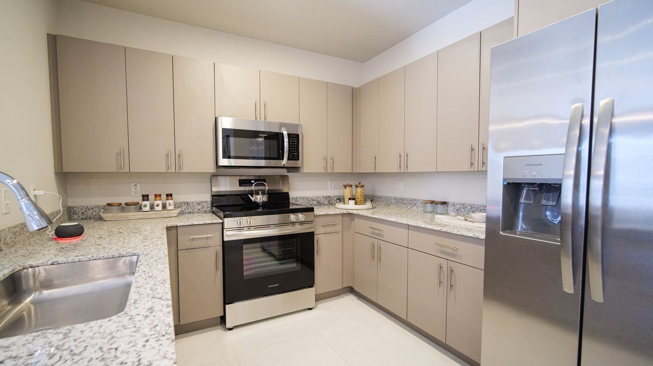 Modern kitchen with beige cabinets, stainless steel appliances, granite counters, and tiled backsplash at Atlantica at Dania Beach apartments in Dania Beach, FL.