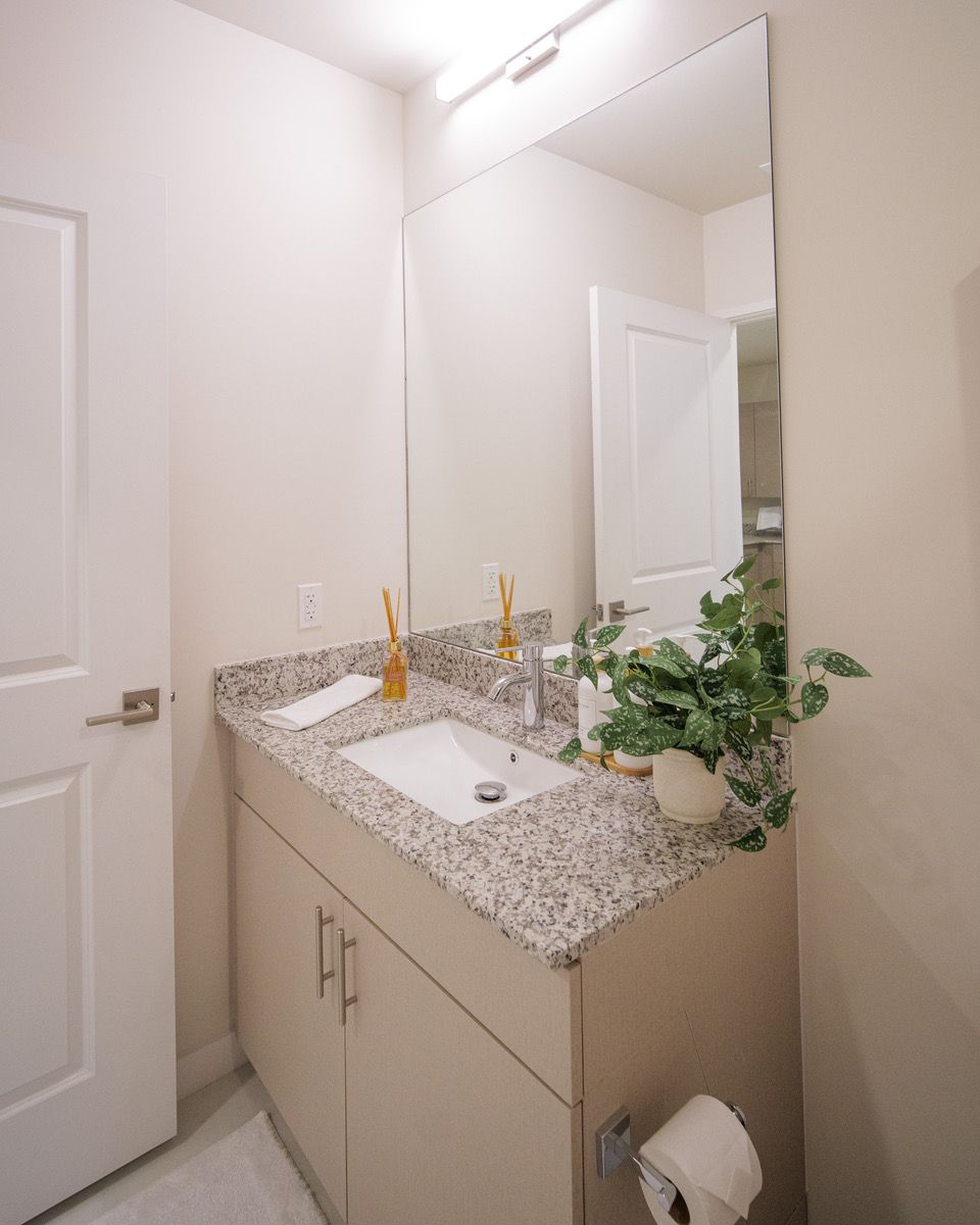 Bright bathroom vanity with speckled countertop, mirror, sink, gold faucet, and a potted plant at Atlantica at Dania Beach apartments in Dania Beach, FL.