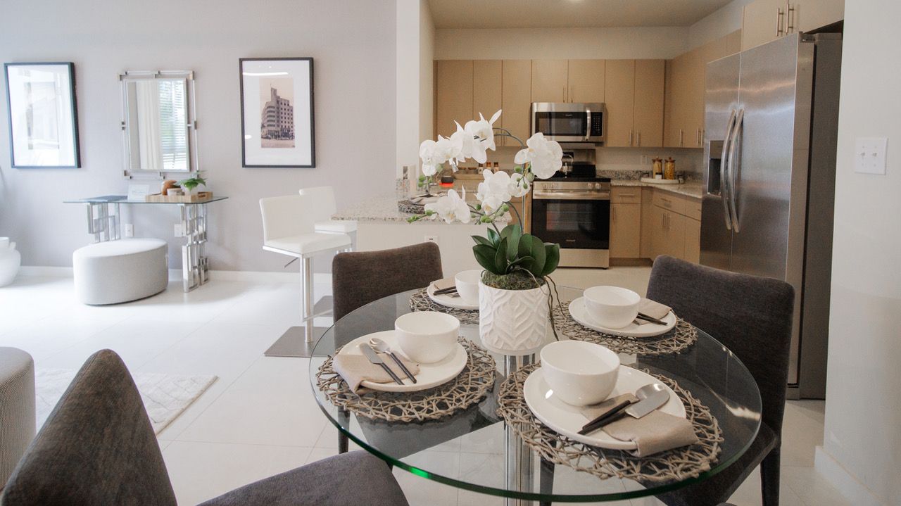 Bright living room and kitchen with a glass table set for tea and white flowers at Atlantica at Dania Beach apartments in Dania Beach, FL.