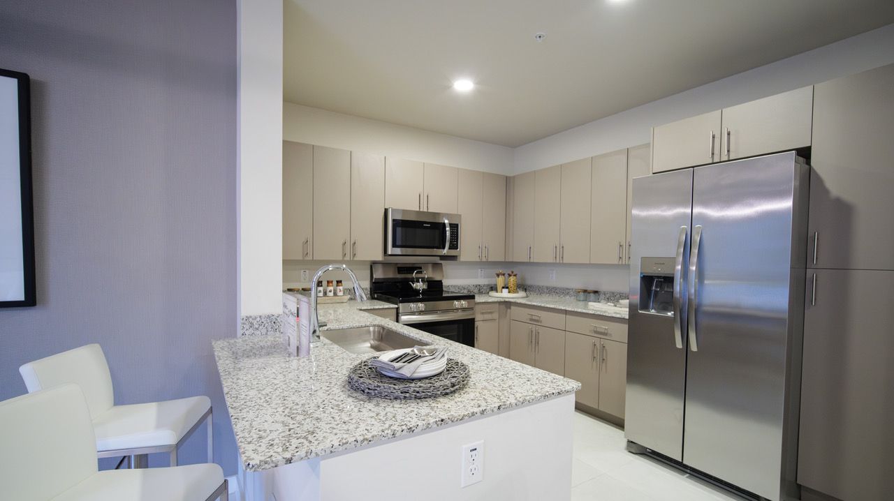 Modern kitchen with stainless steel refrigerator, light cabinets, and granite island countertop at Atlantica at Dania Beach apartments in Dania Beach, FL.