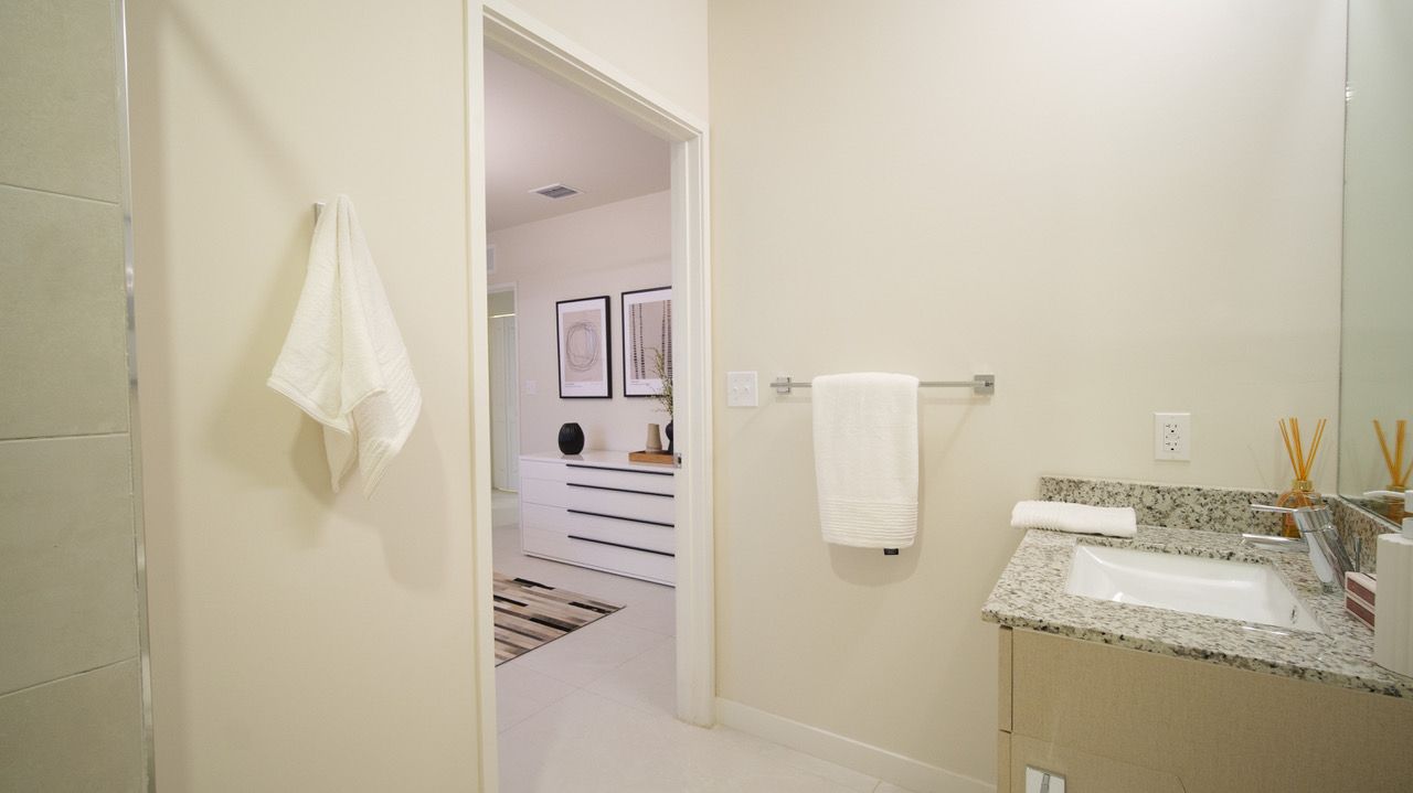 Bright bathroom with sink, towels, and open doorway to a striped bedroom beyond at Atlantica at Dania Beach apartments in Dania Beach, FL.