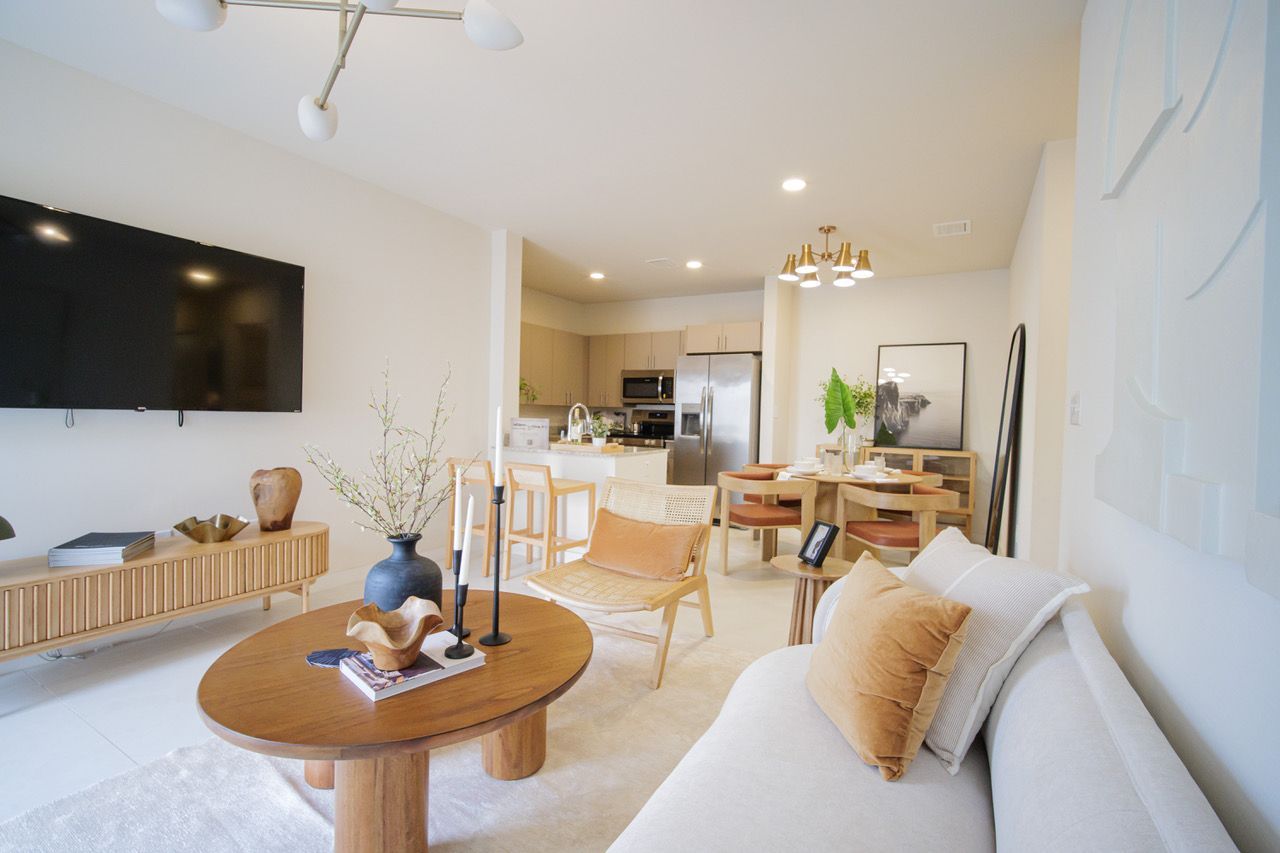 Bright modern living room with white sofa, round coffee table, wall-mounted TV, and open dining area with kitchen beyond at Atlantica at Dania Beach apartments in Dania Beach, FL.