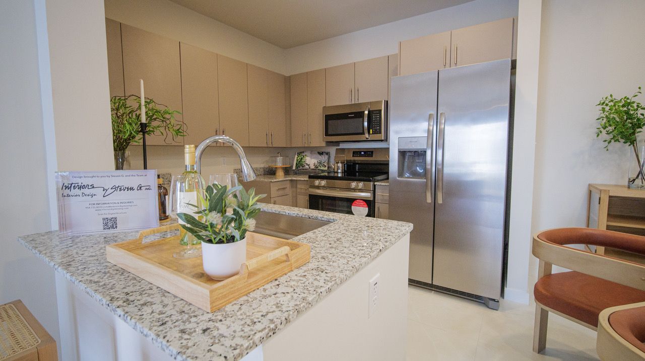 Bright modern kitchen with granite island, stainless steel appliances, and potted plants at Atlantica at Dania Beach apartments in Dania Beach, FL.