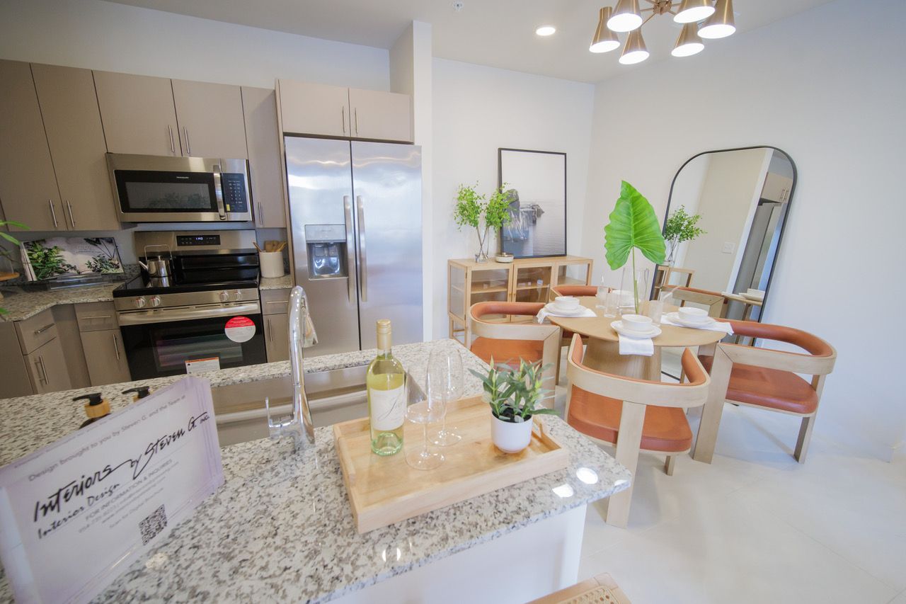 Bright kitchen and dining area with granite counter, stainless fridge, wooden table, and mirror accents at Atlantica at Dania Beach apartments in Dania Beach, FL.