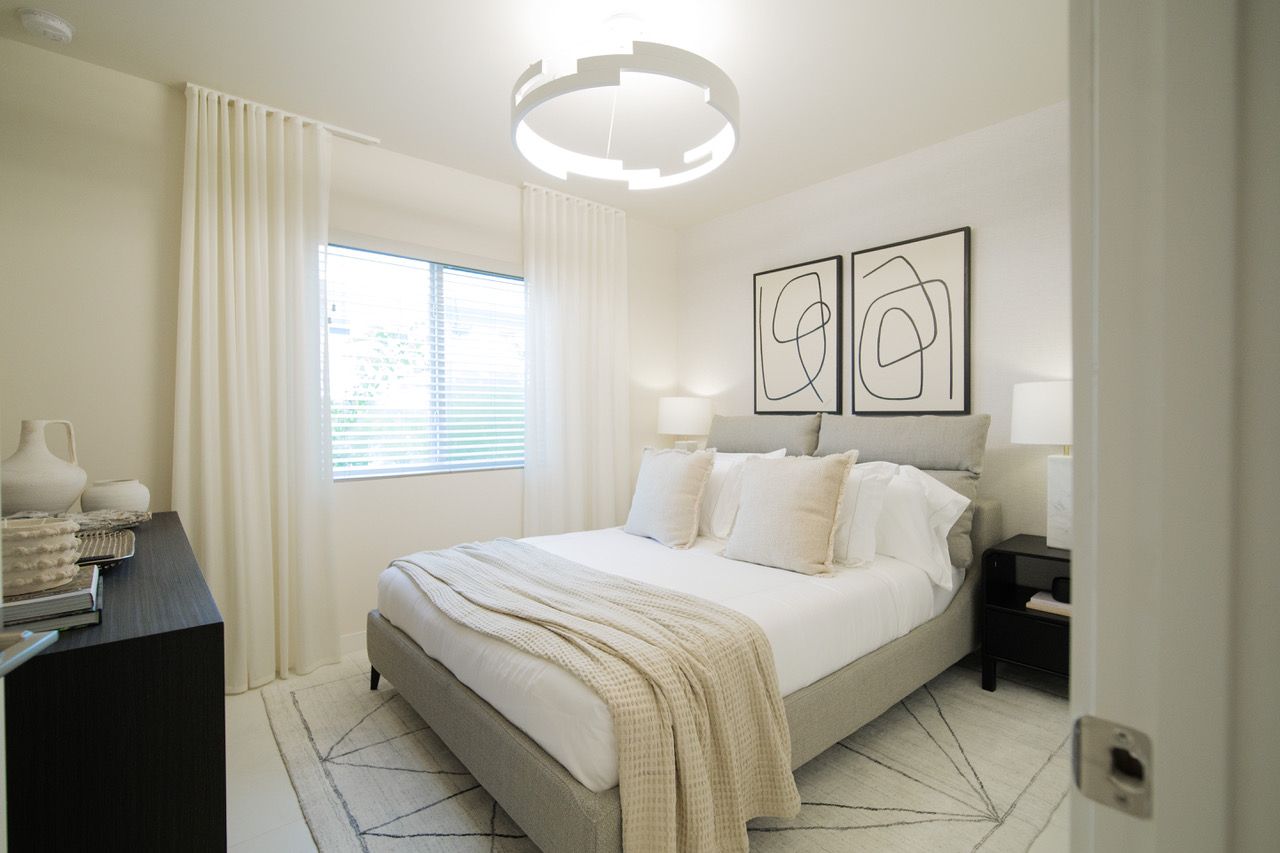 Bright neutral bedroom with a white bed, wall art, window, and soft lighting at Atlantica at Dania Beach apartments in Dania Beach, FL.